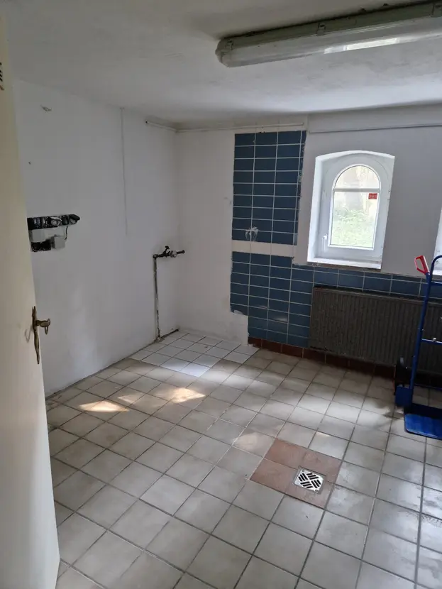 Geflieste Waschküche im Keller mit Bodenablauf und Bogenfenster