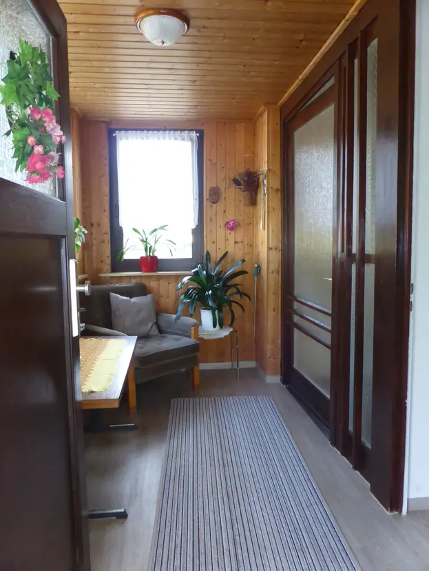Holzverkleidete und verglaste Veranda am Eingangsbereich