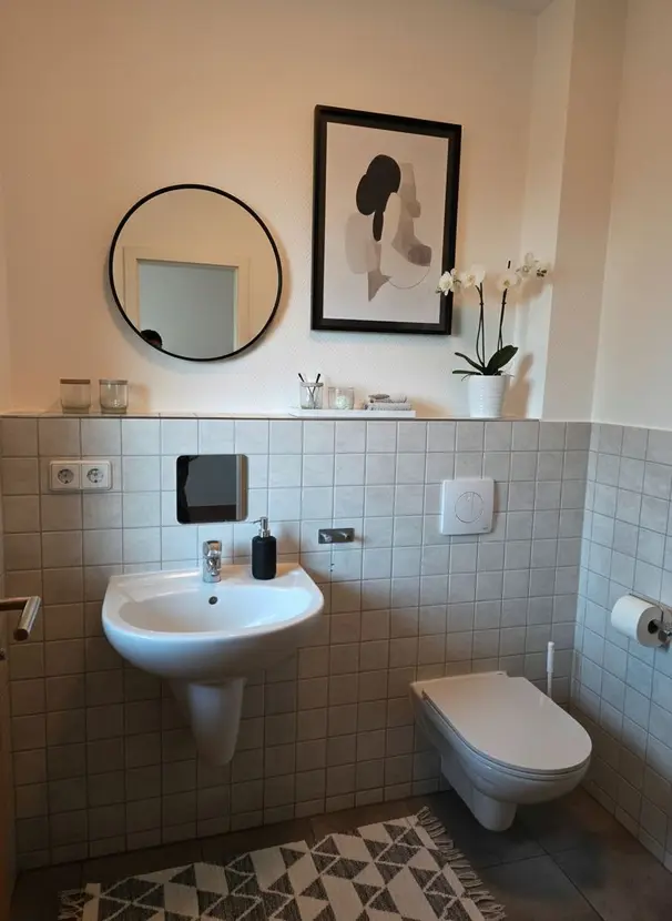 Gäste-WC mit Waschbecken, rundem Spiegel und dezenter Dekoration