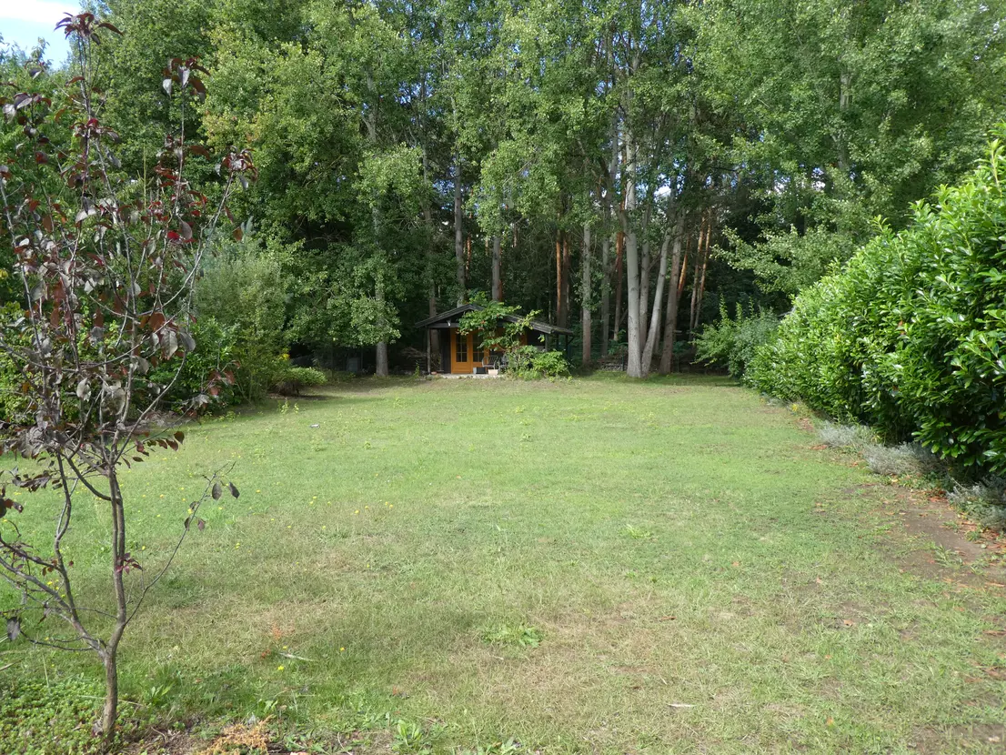 Weitläufiger Garten mit Rasenfläche und Saunahaus am Waldrand
